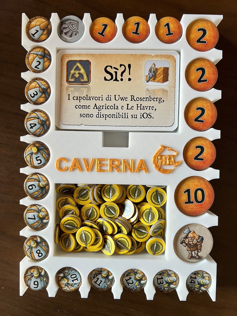 May include: A white plastic game organizer with the words "CAVERNA" and "S&igrave;?!" printed on it. The organizer has slots for different game pieces, including wooden tokens, a card, and a small figure. The organizer is designed for the board game "Caverna: The Cave Farmers".