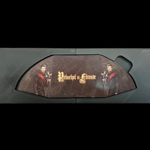 May include: A black box with a hinged lid, open to reveal a game board with two figures in period clothing. The game board is titled "Principi di Firenze".
