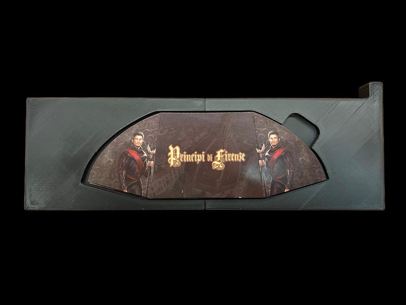 May include: A black box with a hinged lid, open to reveal a game board with two figures in period clothing. The game board is titled "Principi di Firenze".