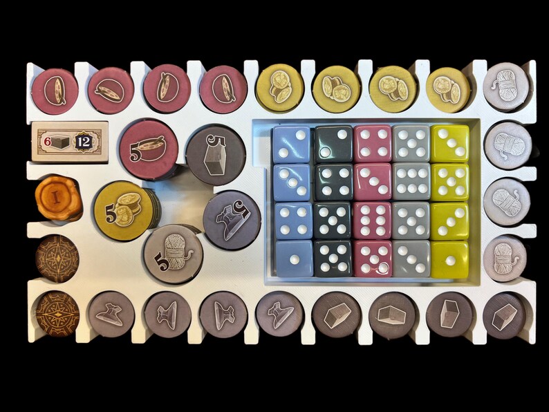 May include: A white organizer with compartments for storing game pieces. The organizer contains various colored dice, small wooden tokens, and small round pieces with numbers and images. The organizer has the numbers 6 and 12 printed on it.