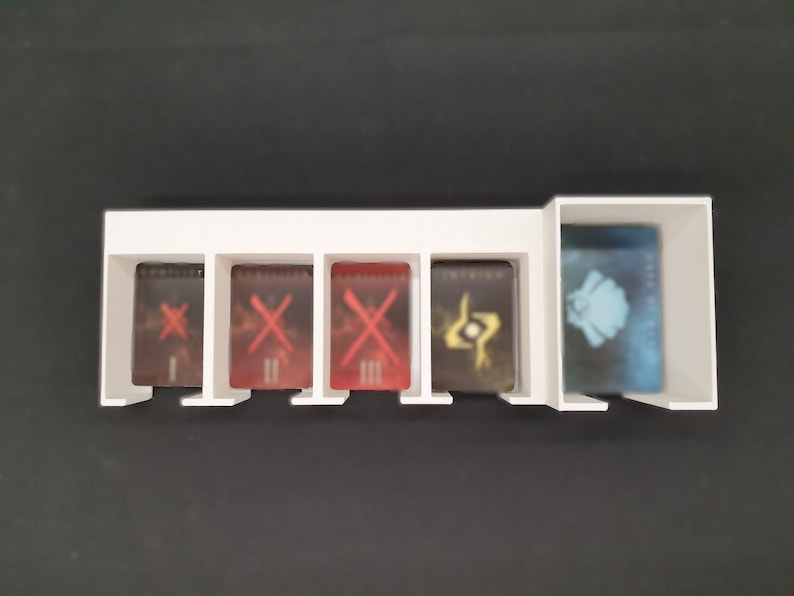 May include: A white plastic card holder with five compartments. Four compartments hold cards with red and gold graphics. The fifth compartment holds a card with a blue and white design. The holder sits on a black surface.