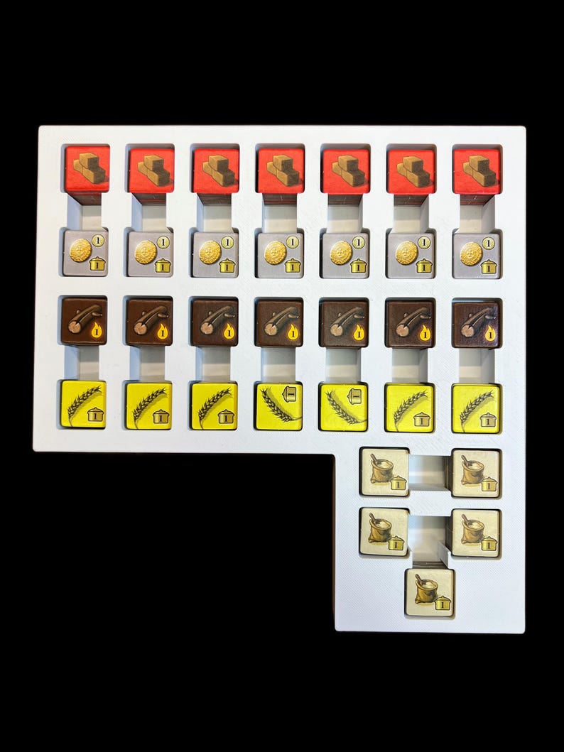May include: A white tray with compartments containing various game pieces. The pieces are small, square, and feature different colors and images, including red bricks, gold coins, brown logs, yellow wheat, and white flour sacks.