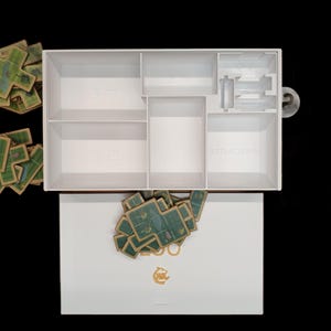 May include: White box with compartments for storing game pieces. The box is open and the compartments are labeled "SET", "ACTION", and "SET". There are stacks of green and brown game pieces outside of the box.