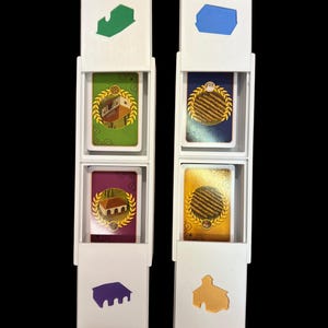 May include: Two white plastic card holders with four cards inside. The cards are yellow, green, purple, and blue. Each card has a different image of a building and a wreath.