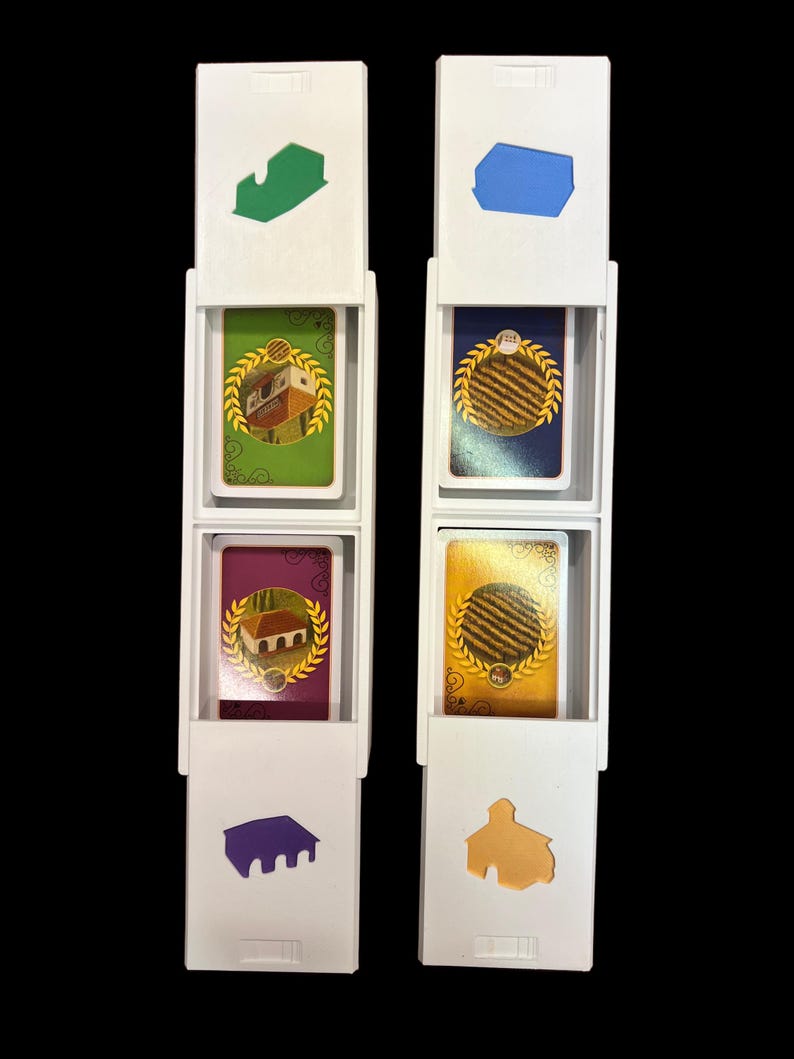 May include: Two white plastic card holders with four cards inside. The cards are yellow, green, purple, and blue. Each card has a different image of a building and a wreath.