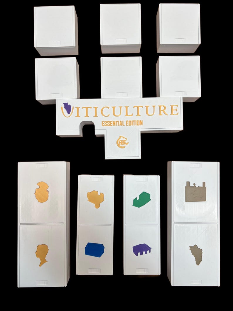 Puede incluir: Piezas de juego blancas con varios s&iacute;mbolos de colores, incluyendo una uva morada, un edificio dorado, un edificio azul, un edificio verde, un edificio morado y un edificio dorado. Las piezas de juego est&aacute;n dispuestas en forma de U con las palabras "VITICULTURE ESSENTIAL EDITION" en letras doradas en una pieza blanca en el centro.
