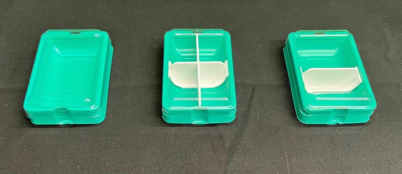 以下が含まれることがあります： 3つの長方形のターコイズ色のプラスチック容器。1つは空で、2つ目は白いインサートと白い紐があり、3つ目は白いインサートがあります。容器は積み重ねられており、リブのデザインになっています。