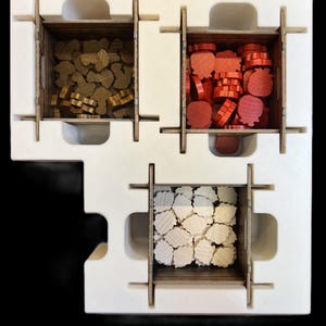 May include: A white foam insert with three compartments for storing game pieces. The compartments are filled with brown, red, and white wooden pieces.