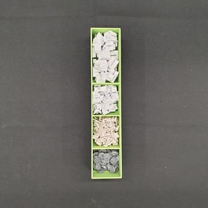 May include: A green plastic organizer with five compartments, each filled with small, gray components. The components vary in shape, including rectangular blocks, irregular shapes, and small, round pieces. The organizer sits on a dark gray surface.
