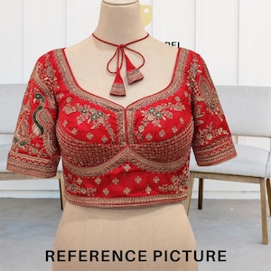 May include: A vibrant red blouse with intricate gold embroidery and a plunging neckline. The short sleeves feature a peacock design. A matching red cord with tassels adorns the neckline. The text "REFERENCE PICTURE" is at the bottom.