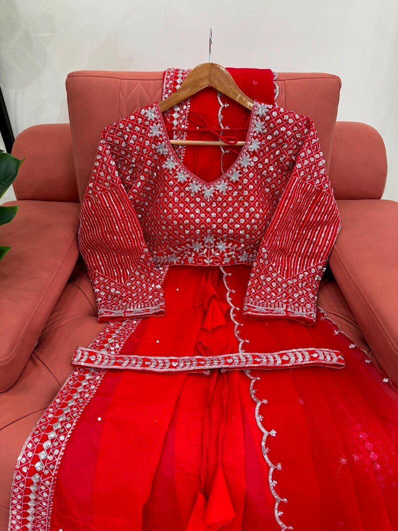 Peut inclure: Un ensemble compos&eacute; d'un chemisier rouge &agrave; manches longues et d'une jupe assortie, orn&eacute; de broderies argent&eacute;es et de sequins. Le chemisier pr&eacute;sente un d&eacute;collet&eacute; en V et des motifs g&eacute;om&eacute;triques, avec une ceinture d&eacute;corative argent&eacute;e.