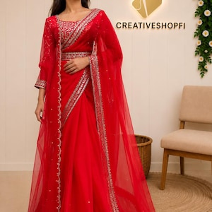 Peut inclure: Un ensemble rouge vif compos&eacute; d'une veste en filet transparent &agrave; manches longues et d'une jupe assortie, toutes deux orn&eacute;es de broderies argent&eacute;es complexes et de sequins le long des bordures. La tenue inclut une ceinture coordonn&eacute;e.