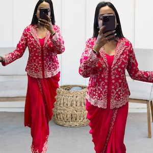 Puede incluir: Conjunto fucsia vibrante con chaqueta y falda drapeada. La chaqueta tiene intrincados bordados dorados en solapas y mangas. La falda es de color liso y fluida. El atuendo es adecuado para ocasiones especiales.