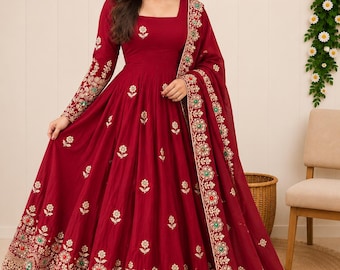 Puede incluir: Un vestido largo de color rojo intenso con escote cuadrado, mangas largas y falda acampanada. El vestido está adornado con bordados florales dorados, pequeños detalles verdes y rojos, y una dupatta transparente a juego con un borde bordado.