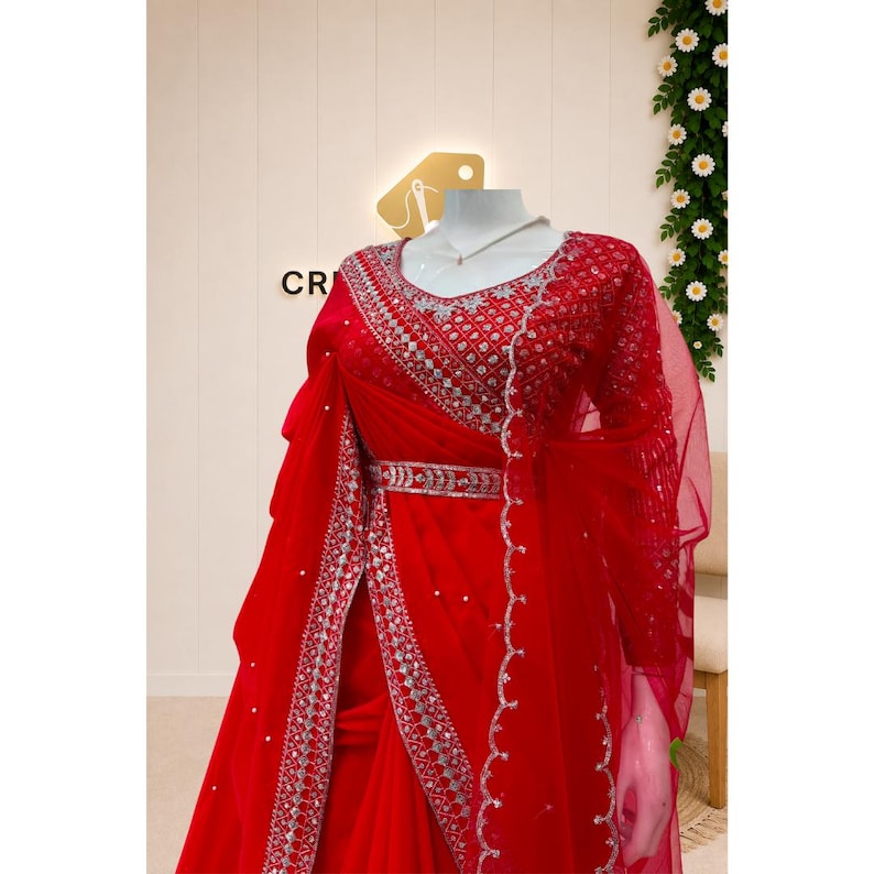 Peut inclure: Une robe rouge vif orn&eacute;e de broderies argent&eacute;es complexes et de miroirs sur l'encolure, le corsage et la ceinture. Le v&ecirc;tement comprend une superposition rouge transparente avec une bordure argent&eacute;e festonn&eacute;e et des perles blanches.