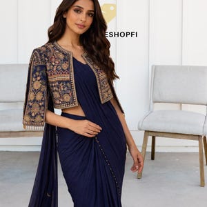 May include: A navy blue saree with a matching embroidered bolero jacket. The jacket features intricate gold and red floral embroidery. The saree is draped elegantly, and the outfit is suitable for formal events.