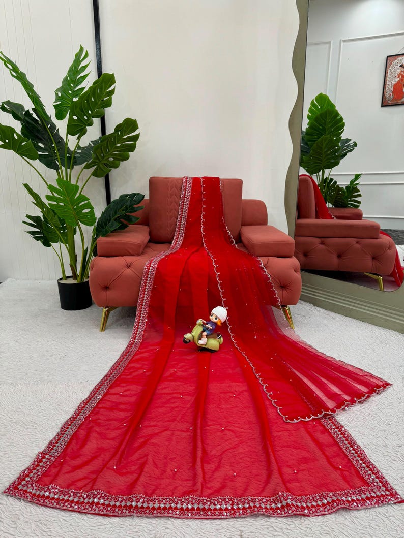 Peut inclure: Un drap&eacute; en tissu rouge vif et transparent, orn&eacute; de broderies argent&eacute;es complexes sur les bordures et de petites d&eacute;corations blanches &eacute;parpill&eacute;es. Le textile est pr&eacute;sent&eacute; &eacute;tal&eacute; sur une surface, agr&eacute;ment&eacute; d'une petite figurine.