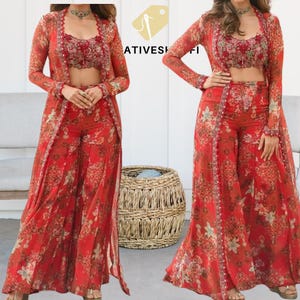 May include: A red floral print three-piece outfit. The set includes a crop top, wide-leg pants, and a long, open-front jacket. The outfit features a delicate floral pattern in shades of red, green, and beige. The fabric appears lightweight and flowing.