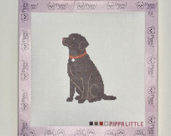 May include: A square needlepoint canvas featuring a dark brown Labrador retriever sitting in the center. The dog wears an orange collar with a white tag. The canvas has a light purple border printed with the text Pippa Little and a dog icon.