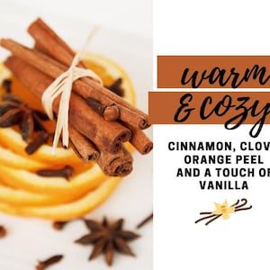 May include: A close-up of cinnamon sticks tied together with twine, resting on top of orange slices. The image also includes star anise and cloves. The text "warm & cozy" is displayed above the image, and the text "CINNAMON, CLOVE, ORANGE PEEL AND A TOUCH OF VANILLA" is displayed below the image.
