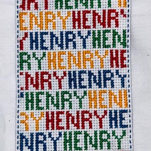Può includere: Un tessuto bianco con il nome "HENRY" ripetuto in un motivo colorato di blu, verde, giallo e rosso.