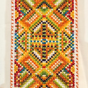 Può includere: Un motivo a punto croce colorato con un design geometrico in tonalità di rosso, arancio, giallo, verde, blu e bianco. Il motivo è incorniciato da un bordo bianco e una bordura arancione.