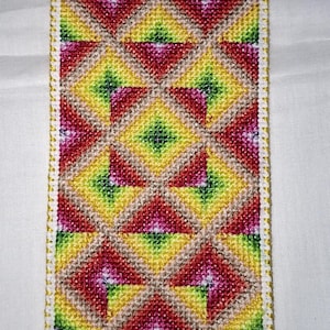 May include: A colorful, handmade bookmark with a geometric pattern. The design features diamond shapes in shades of red, yellow, green, and pink, outlined in white with a gold border. The bookmark is rectangular and appears to be made of cross-stitch.