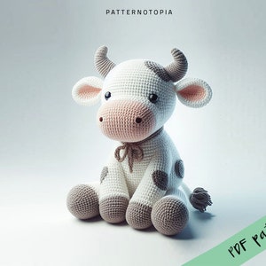 May include: A crocheted white cow with brown spots, sitting with its legs crossed. The cow has a pink nose and a brown ribbon around its neck. The cow is on a white background. PDF pattern.