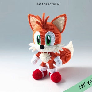 May include: Crocheted plush toy of a red and white fox with a white tail tip. The fox has green eyes and a black nose. The toy is standing on a white surface. "PDF pattern" is written in green text on a white background in the lower right corner of the image.
