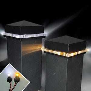 May include: Two black square post caps with clear plastic tops and LED lights. The lights are on and emitting a warm white glow. The caps are mounted on black posts.