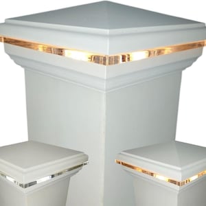 May include: White square post caps with a decorative amber-colored trim. The caps are designed to fit on top of posts, and the trim adds a touch of elegance. The image shows three caps, with the largest one in the center.