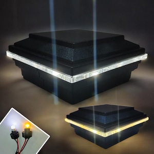 Puede incluir: Dos tapas cuadradas de poste negras con luces LED blancas alrededor del perímetro. Las tapas de poste se muestran sobre un fondo oscuro. Un primer plano de las luces LED muestra una luz blanca y una luz blanca cálida.