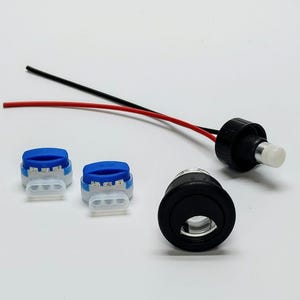 Puede incluir: Un conjunto de componentes eléctricos que incluye una toma de corriente negra, dos conectores de cable azul y blanco y un cable negro y blanco con una tapa blanca.