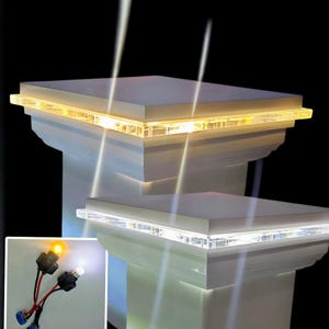 Puede incluir: Dos tapas de poste blancas con luces LED integradas. La tapa superior tiene luces blancas cálidas, y la tapa inferior tiene luces blancas frías. La imagen también muestra dos bombillas LED, una blanca cálida y una blanca fría.