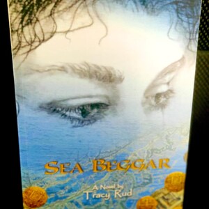 May include: A book cover featuring a close-up of a woman's eye. The title of the book is "Sea Beggar" and the author is "Tracy Rud".