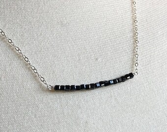 May include: A silver chain necklace with a row of black square beads.