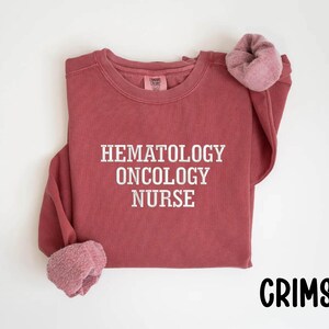 May include: Crimson red sweatshirt with the text "Hematology Oncology Nurse" in white.