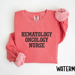 May include: A pink sweatshirt with the text "Hematology Oncology Nurse" in black.
