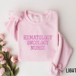 May include: Light pink sweatshirt with the text "Hematology Oncology Nurse" in pink.