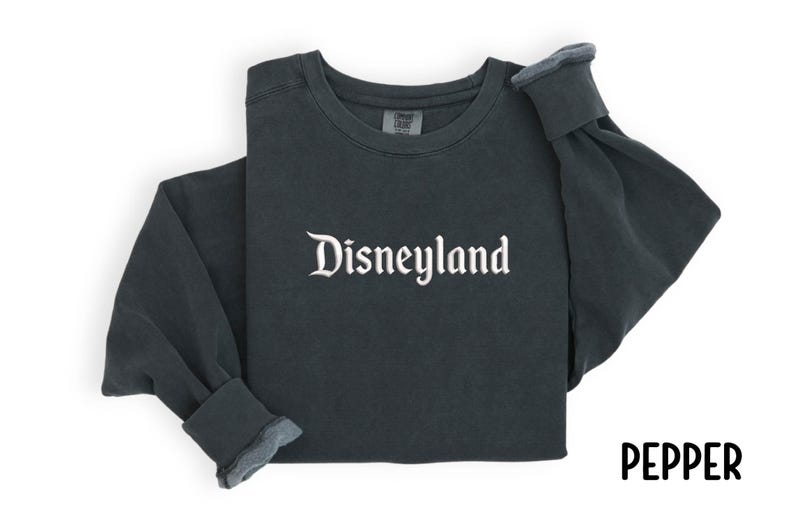 Puede incluir: Sudadera de manga larga gris oscuro con la palabra "Disneyland" en escritura blanca en el pecho. Las mangas est&aacute;n dobladas. La palabra "PEPPER" est&aacute; escrita en escritura negra en la esquina inferior derecha.