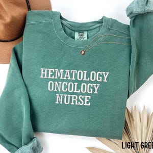 May include: Light green sweatshirt with the text "Hematology Oncology Nurse" embroidered in white.