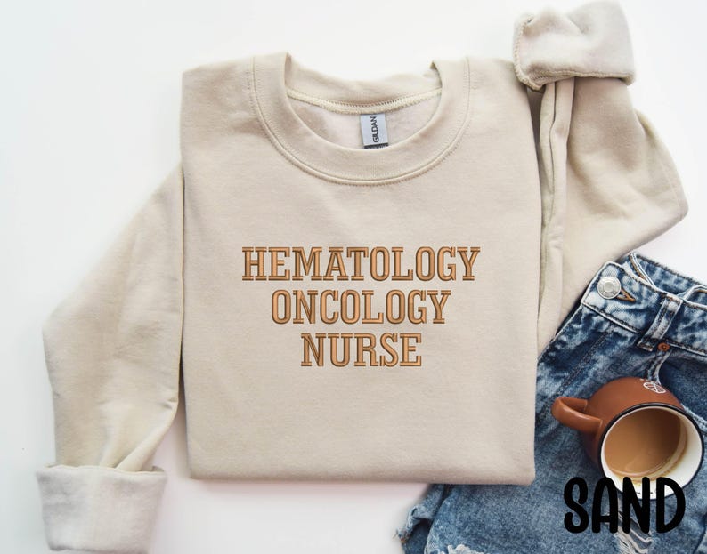May include: A beige sweatshirt with the text "Hematology Oncology Nurse" in brown lettering.