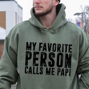 May include: A green hooded sweatshirt with the text "My Favorite Person Calls Me Papi" in black.
