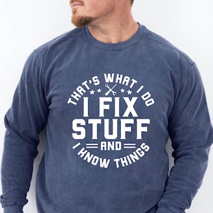 May include: A navy blue sweatshirt with a white graphic that says "That's what I do I fix stuff and I know things". The graphic also includes a wrench and stars.