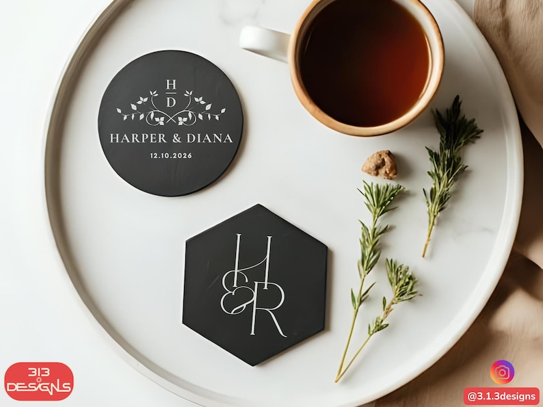 May include: A top-down view of a white tray with a cup of tea, two black coasters, and sprigs of rosemary. One coaster is round with the text "HARPER & DIANA" and the date "12.10.2026". The other coaster is hexagonal with the initials "H & R".