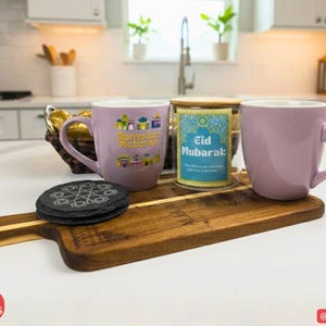 May include: A wooden serving board displays two lavender mugs, a glass jar with an "Eid Mubarak" label, and a black coaster. The mugs have handles and decorative text. The scene is set in a kitchen.
