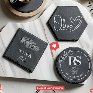 May include: A collection of personalized slate coasters in various shapes: square, hexagon, and round. Each coaster features custom white text and designs, including names, initials, and botanical elements. The coasters are arranged on a marble serving board.
