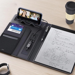 May include: Black leather business organizer with a built-in phone stand, credit card slots, and a pen. A smartphone displays a video call. A notebook with handwritten notes and a coffee cup are also visible.