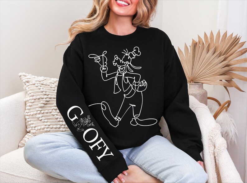 K&ouml;nnte beinhalten: Schwarzes Sweatshirt mit einer wei&szlig;en Strichzeichnung von Goofy. Das Wort "GOOFY" ist vertikal auf dem linken &Auml;rmel aufgedruckt. Das Design zeigt Goofy in einer dynamischen Pose, mit einem verspielten Cartoon-Stil.