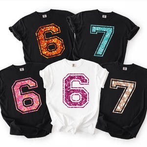 May include: Five black and white t-shirts with glittery numbers 6 and 7. The numbers are in orange, teal, pink, purple, and champagne colors. The shirts are likely for a birthday or special occasion.